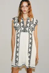 Vestido corto blanco de Zara Woman Collection con bordados en contraste de color negro, escote en V y mangas sisa con pequeños volados.