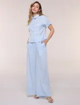 Conjunto de dos piezas confeccionado en lino, de estilo casual safari. Incluye camisa de manga corta con cuello camisero con bordado festoneado, abotonadura frontal y bolsillos en el pecho; y pantalón palazzo de tiro alto con bolsillos y cinturón con hebilla metálica dorada.