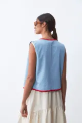 Chaleco celeste de denim con terminaciones en crochet rojo.
