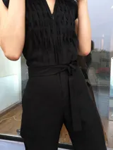 Mono largo de lino color beige, con detalle plisado en el frente, escote en V, sin mangas, lazo en la cintura, cierre invisible delantero y bolsillos laterales.