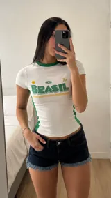 Remera tipo top ajustada, color blanco con detalles en verde y amarillo, cuello redondo y mangas cortas, con diseño estampado frontal con la palabra "BRASIL".