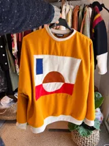 Buzo de calce relajado color maíz, confeccionado en friza de verano, con intervención artesanal en el pecho que presenta una composición abstracta de piezas textiles cosidas a mano en tonos blanco, rojo, azul y terracota.