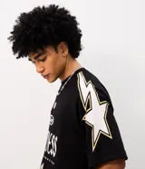 Remera oversized de poliéster calado estilo mesh, color negro con detalles en blanco y dorado, cuello redondo y mangas cortas. Presenta estampa frontal localizada, numeración y estrellas aplicadas en los hombros.