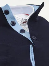 Buzo azul marino de algodón con cuello doble abotonado y ribete rojo en cuello, puños y ruedo.