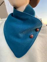 Cuello tipo bufanda de lana procesada en color azul petróleo, con diseño triangular y cierre mediante dos botones forrados en cuero marrón.