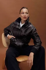 Chaqueta de cuero estilo bomber en color negro, con cuello alto, cierre frontal con cremallera y solapa con botones a presión. Presenta puños y cintura de tejido elástico acanalado, bolsillos laterales y un diseño estructurado.