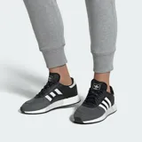 Championes Adidas Marathon Tech, modelo de estilo retro con combinación de colores negro y gris. Presenta las icónicas tres tiras laterales en blanco, puntera reforzada y entresuela con tecnología Boost que ofrece amortiguación y retorno de energía.