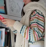 Sweater de punto artesanal, color crudo, con cuello tortuga y diseño de franjas horizontales con detalles en tonos rosado, celeste, verde oscuro y mostaza.
