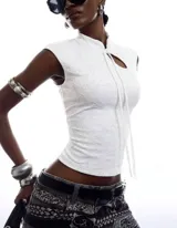 Top blanco de encaje floral con diseño de inspiración oriental, corte al cuerpo, cuello alto, abertura frontal con lazo para anudar y mangas cortas.