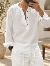 Camisa de muselina blanca de corte slim, con cuello mao y cierre frontal parcial de botones de madera. Presenta mangas largas con puños ajustables y dobladillo redondeado.