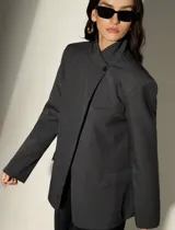 Blazer sastrero de corte oversized en color gris oscuro, con hombros estructurados, cuello mao y cierre frontal cruzado con un botón. Presenta bolsillos laterales con solapa y un bolsillo superior en el pecho.
