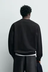 Sudadera de cuello redondo y manga larga, confeccionada en algodón con interior afelpado. Presenta un diseño de corte regular con estampado de texto en contraste en la parte frontal y acabados en rib en puños y ruedo.