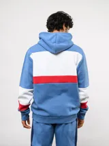 Canguro con capucha de Umbro del Club Nacional de Football, con diseño de bloques de color en azul, blanco y rojo. Presenta bolsillo frontal tipo canguro, cordones ajustables en la capucha y logos bordados del club y la marca.