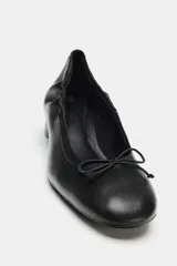 Zapato tipo bailarina de piel color negro, con tacón bloque bajo, puntera redonda y detalle de pequeño lazo en la parte delantera.