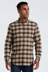 Camisa de manga larga confeccionada en tela de franela con estampado de cuadros en tonos marrones, beige y líneas azules. Presenta cuello clásico abotonado, cierre frontal con botones y un bolsillo pequeño en el pecho.