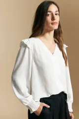 Camisa negra de manga larga con escote en V y cierre frontal de botones. Presenta detalles de volados en los hombros, frunces en la espalda y puños elastizados que le otorgan una silueta relajada y fluida.