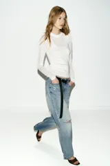 Jeans de tiro bajo, corte recto y pierna ancha, color celeste claro desgastado. Presenta roturas visibles en la zona de la rodilla y pequeños desgastes en los muslos y bolsillos.