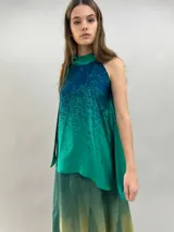 Blusa de satén con escote halter y cuello elevado anudado lateralmente. Presenta un diseño estampado degradado en tonos verde esmeralda y azul, con corte holgado y caída fluida.