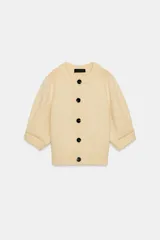 Chaqueta de punto color amarillo claro, con cuello redondo, mangas abullonadas por debajo del codo y cierre frontal con botones oscuros.