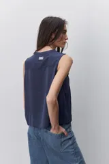 Blusa sin mangas color negro, de silueta fluida, con cuello redondo, detalle de alforzas en el frente y abotonadura parcial con botones visibles.