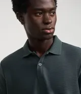 Camisa polo de corte regular, color verde oscuro, confeccionada en tejido texturizado. Presenta cuello clásico con botones frontales y mangas cortas.