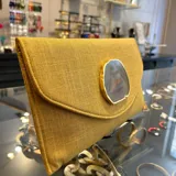 Sobre de fiesta color mostaza, hecho artesanalmente en la India, con aplique de piedra ágata a tono. Incluye asa de cadena dorada para llevar al hombro.