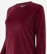 Pijama de dos piezas confeccionado en plush con textura acanalada y estampado de corazones en relieve. Incluye una blusa de cuello redondo con mangas largas y puños ajustados, y un pantalón con cintura elástica y puños en el ruedo.