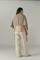 Chal de lana fina sin teñir con diseño de cuadros sutiles, cierre frontal con alamar y bolsillos de cuero metalizado. Presenta terminaciones con flecos en el ruedo y un calce estructurado en los hombros.