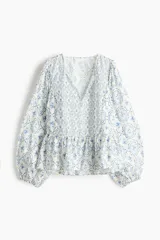 Blusa en mezcla de viscosa con peplum acampanado, cuello redondo, escote en V y tiras finas con cuentas decorativas. Presenta mangas globo largas con elástico en los puños y un estampado en tonos blancos y azules con motivos florales y geométricos.
