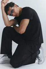 Pantalón deportivo negro de corte estándar y piernas rectas, confeccionado en tejido funcional ripstop con tecnología DryMove™. Cuenta con cintura elástica con cordón de ajuste oculto, bolsillos laterales con cierre y detalles perforados en las piernas.