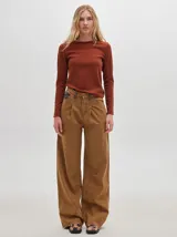 Pantalón jean de tiro alto y corte pinzado, con perneras de caída suelta y levemente anchas en el bajo. Posee pasador con hebilla en la parte trasera.