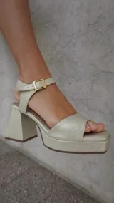 Sandalias doradas con plataforma y taco cuadrado, tira delantera y tobillera con hebilla.