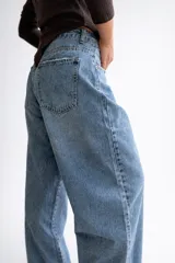 Pantalón de jean estilo palazzo en tono celeste medio, con corte amplio y tiro medio. Presenta sutiles detalles de roturas en los bolsillos y en el ruedo deshilachado.