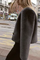Chaqueta de cuello redondo y manga larga con tejido exterior efecto pelo e interior efecto ante. Presenta bolsillos delanteros de vivo y cierre frontal con alamares metálicos.