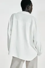 Camisa de cuello solapa y escote en pico, manga larga con puños y detalle de pliegues en el delantero. Presenta un diseño de bajo asimétrico.