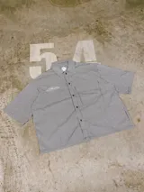 Camisa de manga corta con corte híbrido boxy fit/oversize, confeccionada en algodón. Disponible en tres diseños: a cuadros marrones, a rayas blancas y negras, y a rayas burdeos y blancas. Presenta bordados de diseño propio de la marca.