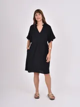 Vestido midi de color negro con cuello en V y mangas cortas tipo kimono. Presenta un corte holgado con cintura ligeramente marcada y falda con vuelo.
