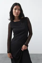 Vestido largo de manga larga confeccionado en tejido de malla transparente con sutil textura. Presenta un diseño entallado, cuello redondo y una silueta estilizada.