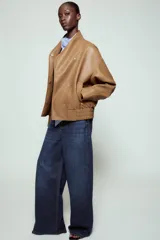 Chaqueta bomber ZW Collection confeccionada en tejido efecto piel de color marrón. Cuenta con cuello subido, manga larga con puño y botón a presión, bolsillos delanteros y bajo recto elástico. Cierre frontal cruzado con botones a presión.