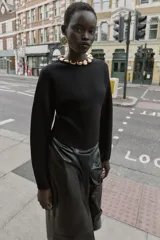 Jersey negro de cuello redondo con aplicación de bolas metálicas doradas, manga larga y bajo asimétrico. Cierre en la espalda con abertura y botón.