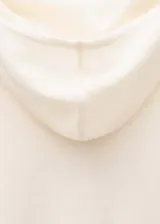 Buzo de punto fino color crema, con cuello redondo, manga larga con aberturas para el pulgar y diseño recto.