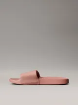 Ojotas tipo slide Calvin Klein Jeans, color rosado, con banda superior de lona de algodón reciclado y logo de la marca estampado en blanco. Presentan suela de EVA con plantilla ergonómica moldeada.