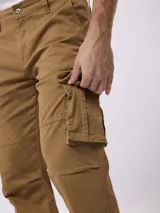 Pantalon cargo de gabardina color tostado, con bolsillos laterales tipo cargo, bolsillos frontales y traseros, cierre de botón y cremallera.