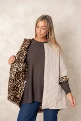 Campera acolchada de corte amplio y largo midi, color beige con diseño capitoneado. Presenta mangas tres cuartos con puños vueltos que revelan un interior estampado con motivo animal print. Diseño sin cuello y cierre frontal oculto.