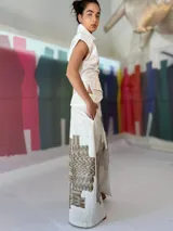 Falda larga blanca de lino y algodón con estampa exclusiva en cobre laminado. Corte asimétrico, tajo central y un bolsillo lateral. Cierre frontal con broches a presión.