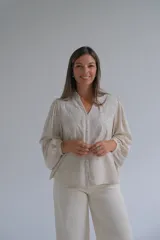 Blusa de color beige con cuello mao, cierre frontal con botones y mangas largas abullonadas. Presenta delicados bordados florales en la parte superior delantera.