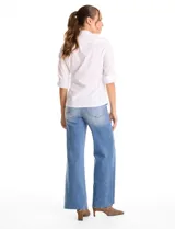 Camisa blanca de algodón con cuello solapa, escote en V y cierre frontal con botones decorativos de strass. Presenta pinzas de entalle para un ajuste definido, mangas tres cuartos con terminación rebatible y ruedo redondeado.