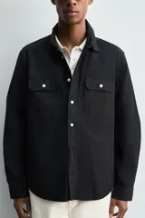 Sobrecamisa de corte relajado confeccionada en tejido ligero de algodón color negro. Presenta cuello de solapa, manga larga con puños abotonados y dos bolsillos de plastrón con solapa en el pecho. Cuenta con cierre frontal de botones a contraste y aberturas laterales en el bajo.