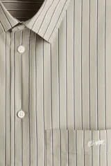 Camisa de popelina de algodón con cuello inglés, tapeta clásica y bolsillo superior abierto. Presenta un canesú en la espalda y mangas largas con puños abotonados. El bajo es levemente redondeado.