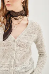 Cardigan de punto calado en color beige, con escote en V y cierre frontal de botones. Presenta un diseño de textura con franjas horizontales y mangas largas.